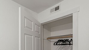 Una puerta blanca con una pequeña rejilla encima, un ventilador blanco en una esquina y un suelo de madera.