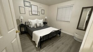 Un dormitorio con cama, mesitas de noche, un espejo y una ventana con persianas.