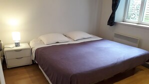 Ein Schlafzimmer mit Bett, Nachttisch, Lampe und einem Fenster mit Vorhängen.