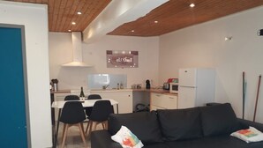 Ein modernes Wohnzimmer mit einer schwarzen Couch, einem Essbereich mit einem weißen Tisch und Stühlen sowie einer Küche mit weißen Geräten.