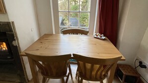 A room with a wooden table and chairs, a window with a view of greenery, and a fireplace. - Robinson’s Cottage in Cockermouth quiet and central (Cockermouth)