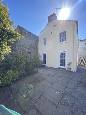 A two-story building with a stone wall on one side and a paved courtyard.
