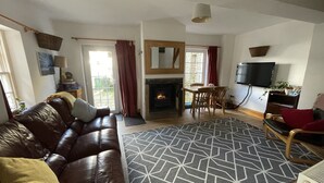 A living room with a leather sofa, a fireplace, a dining area, and a TV mounted on the wall. - Robinson’s Cottage in Cockermouth quiet and central (Cockermouth)