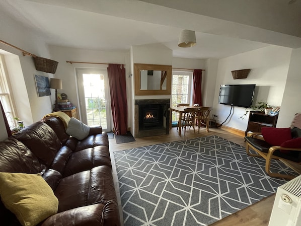 A living room with a leather sofa, a fireplace, a dining area, and a TV mounted on the wall.