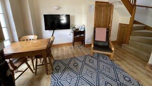 A living room with a wooden dining table, a TV mounted on the wall, a patterned rug, and a staircase. - Robinson’s Cottage in Cockermouth quiet and central (Cockermouth)