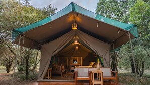 Un hébergement sous tente doté d’une terrasse en bois, d’un coin repas et offrant une vue sur la forêt environnante.