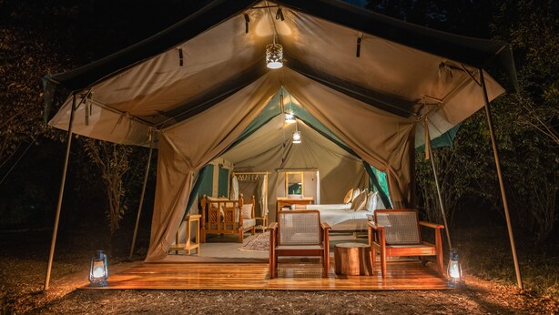 Une tente dotée d’une terrasse en bois, d’un lit et de deux chaises.