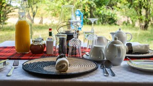 Une table dressée à l’extérieur, avec différents types de verres, une bouteille de jus de fruits et tout le nécessaire pour un pique-nique.