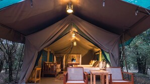 Une tente équipée d’un lit, de deux chaises, d’une table et d’un luminaire suspendu.