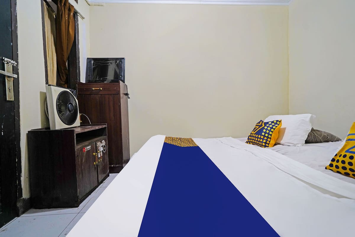 A bedroom with a bed, a wooden wardrobe, a television, and a fan.