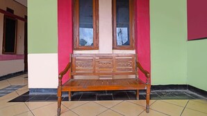 A wooden bench with a backrest and armrests, positioned in front of a window with a view of a utility pole. - SPOT ON 91783 Urban Syariah ResidenceNearGOR Pandawa Lima (Bandung)