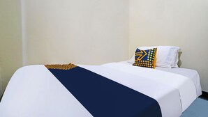 A single bed with a white and navy blue bedspread, a navy blue pillow with yellow geometric patterns, and a white pillow. - SPOT ON 91783 Urban Syariah ResidenceNearGOR Pandawa Lima (Bandung)