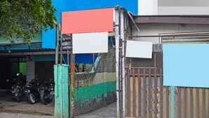 A gated area with a motorcycle parked inside, a green tree, and a building with a blue and white facade. - SPOT ON 91783 Urban Syariah ResidenceNearGOR Pandawa Lima (Bandung)