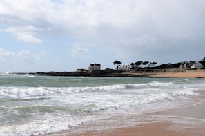 A beach with waves, a rocky outcrop, and a building with trees. - Grand Appartement REZ DE Jardin, 100m Dela Plage (Batz-sur-Mer)
