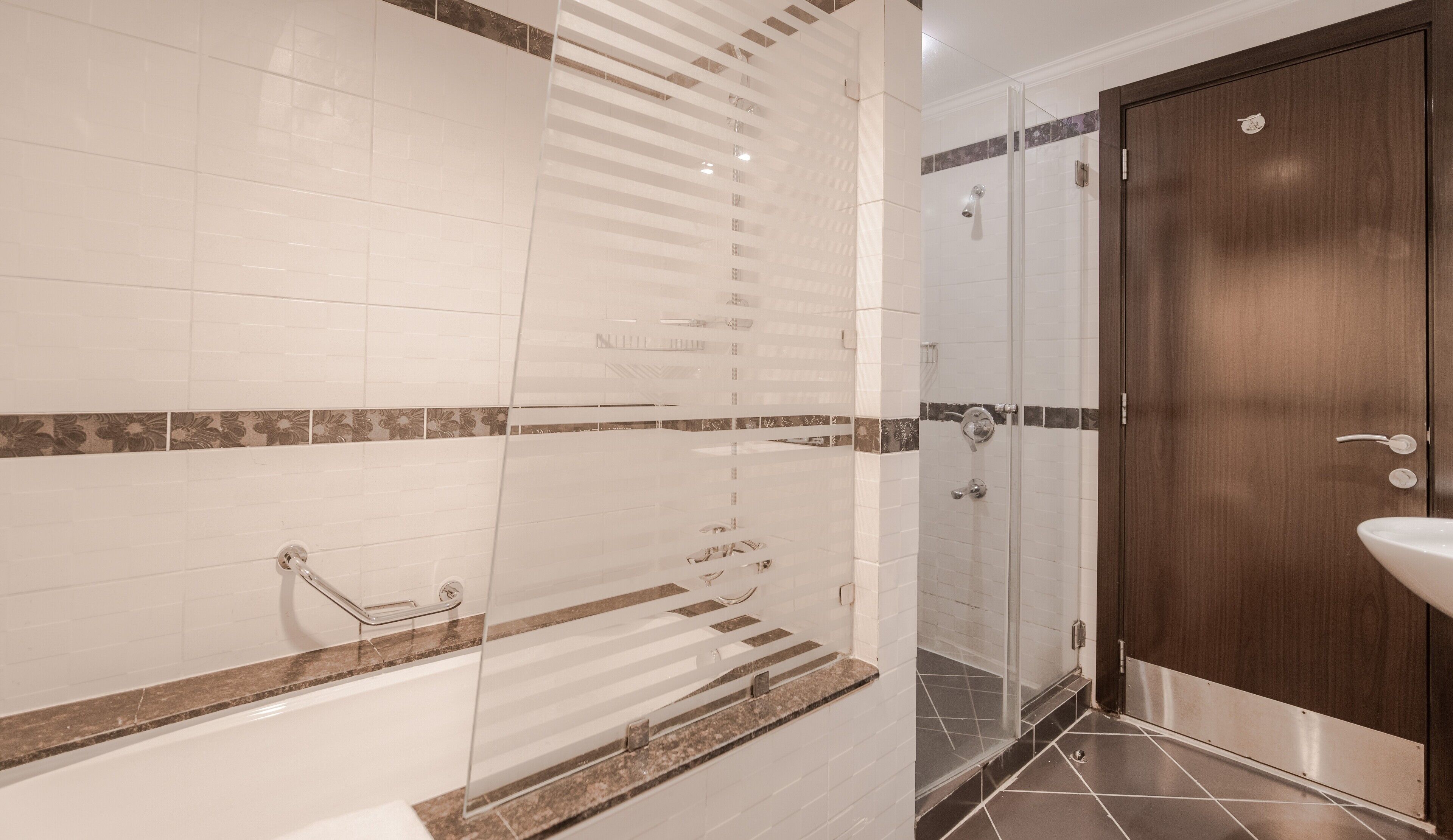 A modern bathroom with a glass shower enclosure, a wooden door, and a marble countertop.