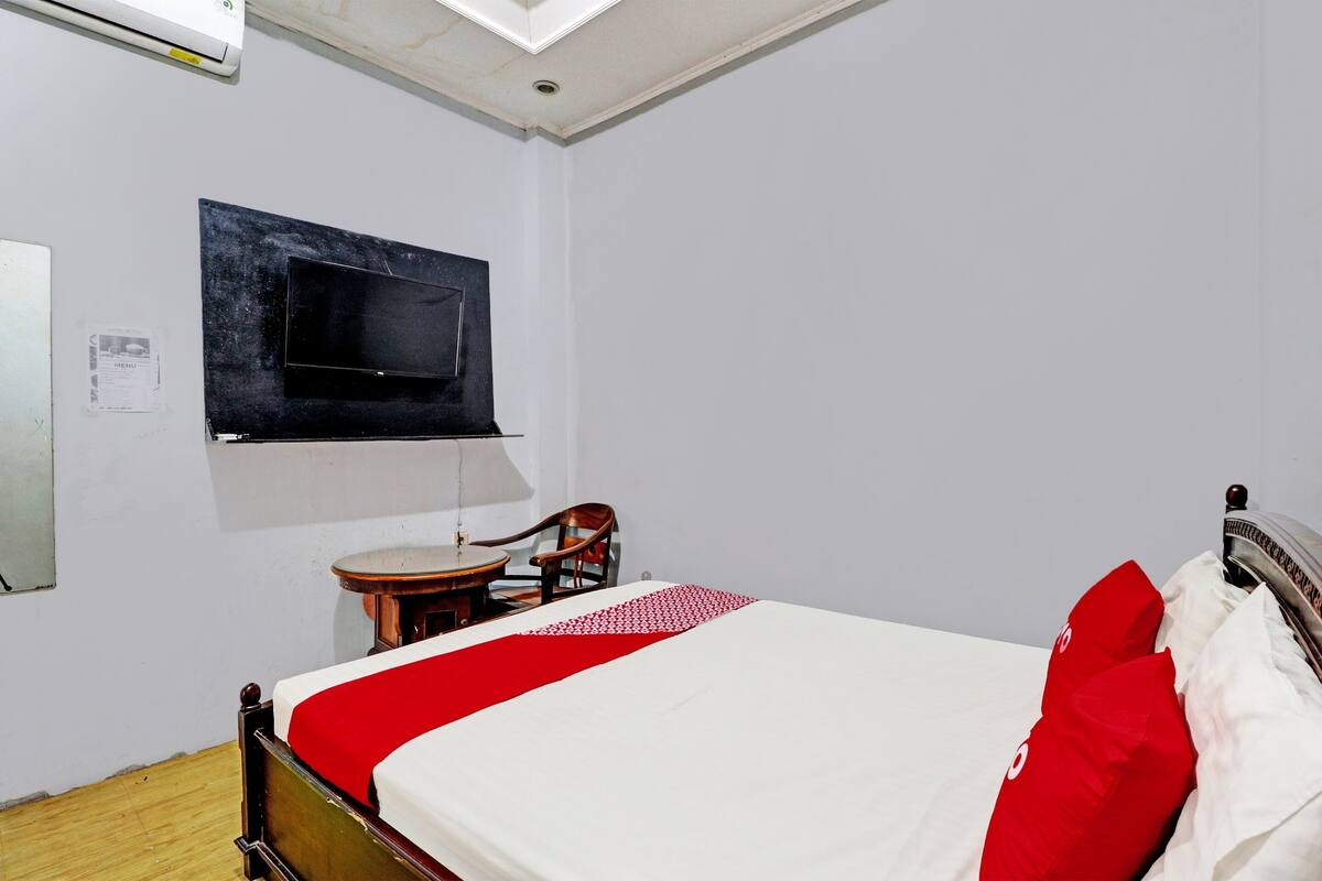 A bedroom with a bed, a desk, a chair, a TV mounted on the wall, and a ceiling fan.