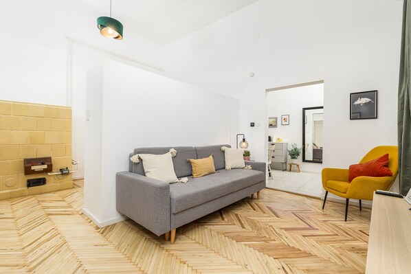 A modern living room with a grey sofa, yellow armchair, and a herringbone wooden floor.