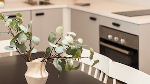 A modern kitchen with white cabinetry, a black dining table, and a vase with green leaves. - Venus Apartments - King street IV (Budapest)