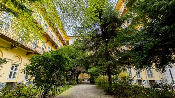 A pathway flanked by lush greenery and yellow buildings with balconies. - Venus Apartments - King street IV (Budapest)