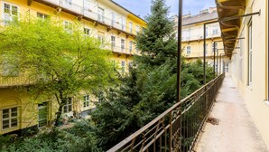 A multi-story yellow building with balconies, surrounded by greenery and a metal railing. - Venus Apartments - King street IV (Budapest)