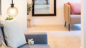 A modern living room with a grey sofa, a hanging lamp, and a large mirror reflecting a dining area. - Venus Apartments - King street IV (Budapest)
