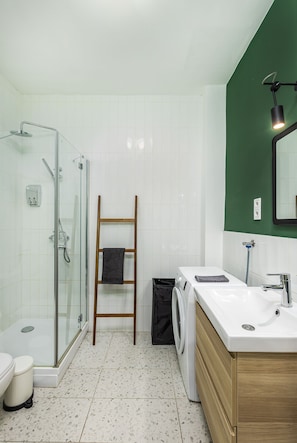 Un baño moderno con cabina de ducha de vidrio, una escalera de madera, una lavadora y un lavabo con espejo.