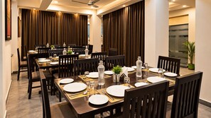 Un espace repas avec plusieurs tables dressées pour les repas, doté de meubles en bois foncé et d’une décoration moderne.