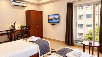 A hotel room with two beds, a desk, a chair, a TV, a wardrobe, and a window with curtains.