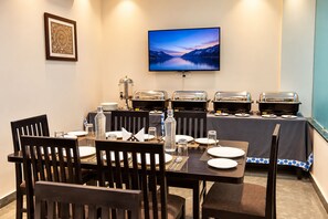 Un comedor con mesas de buffet, un televisor montado en la pared y una obra de arte enmarcada.