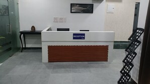 A reception desk with a sign, air conditioning units, a framed picture, and a chair. - The Altruist New Town Hotel (Barasat)