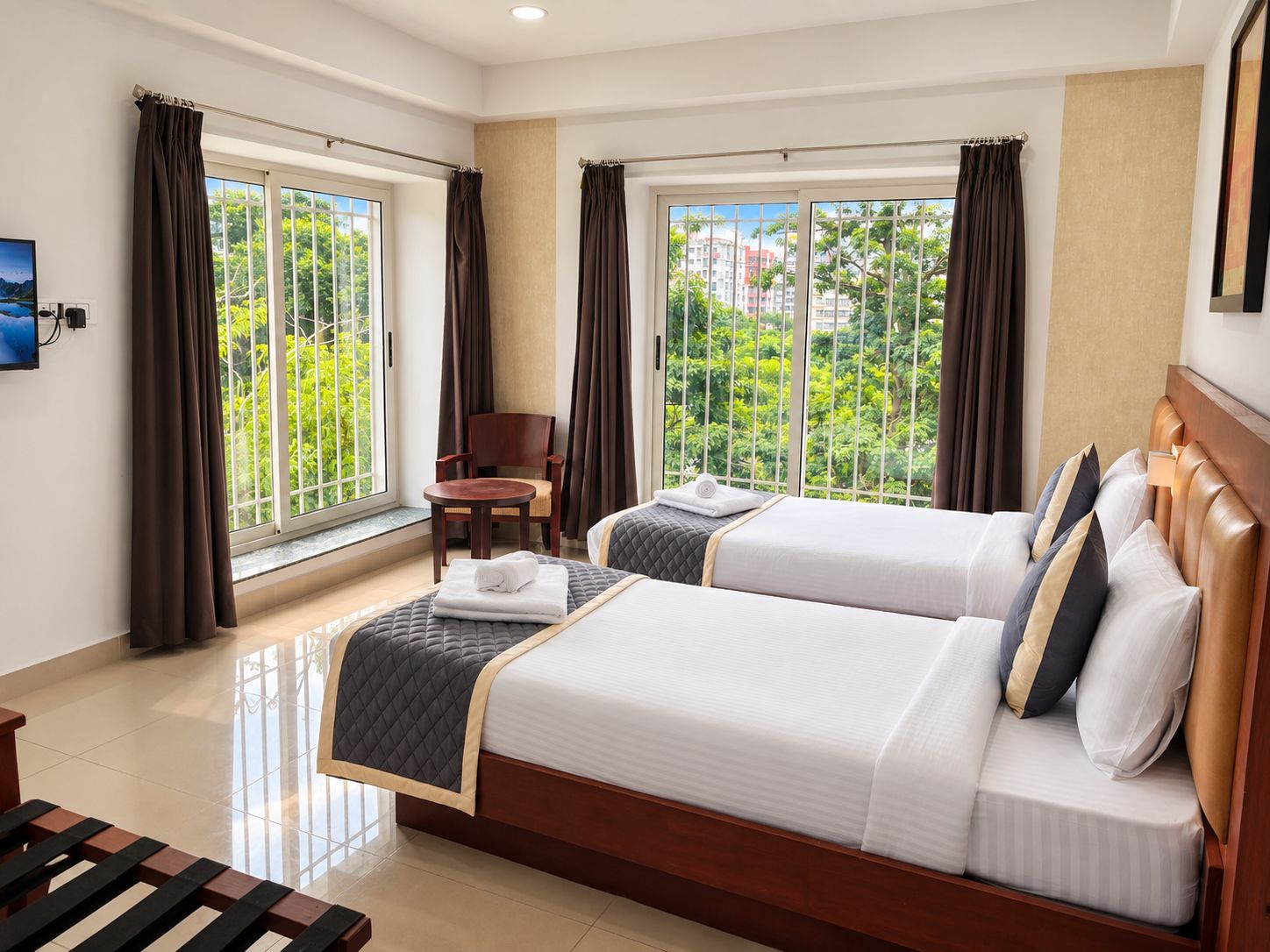 A hotel room with two beds, a chair, a table, and large windows with curtains.