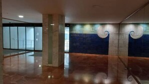 Een ruime lobby met een gepolijste marmeren vloer, een glazen lift en een decoratieve wand met een blauw-wit patroon.
