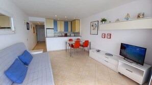 Een moderne woonkamer met een bank, een televisie en een eethoek met stoelen.