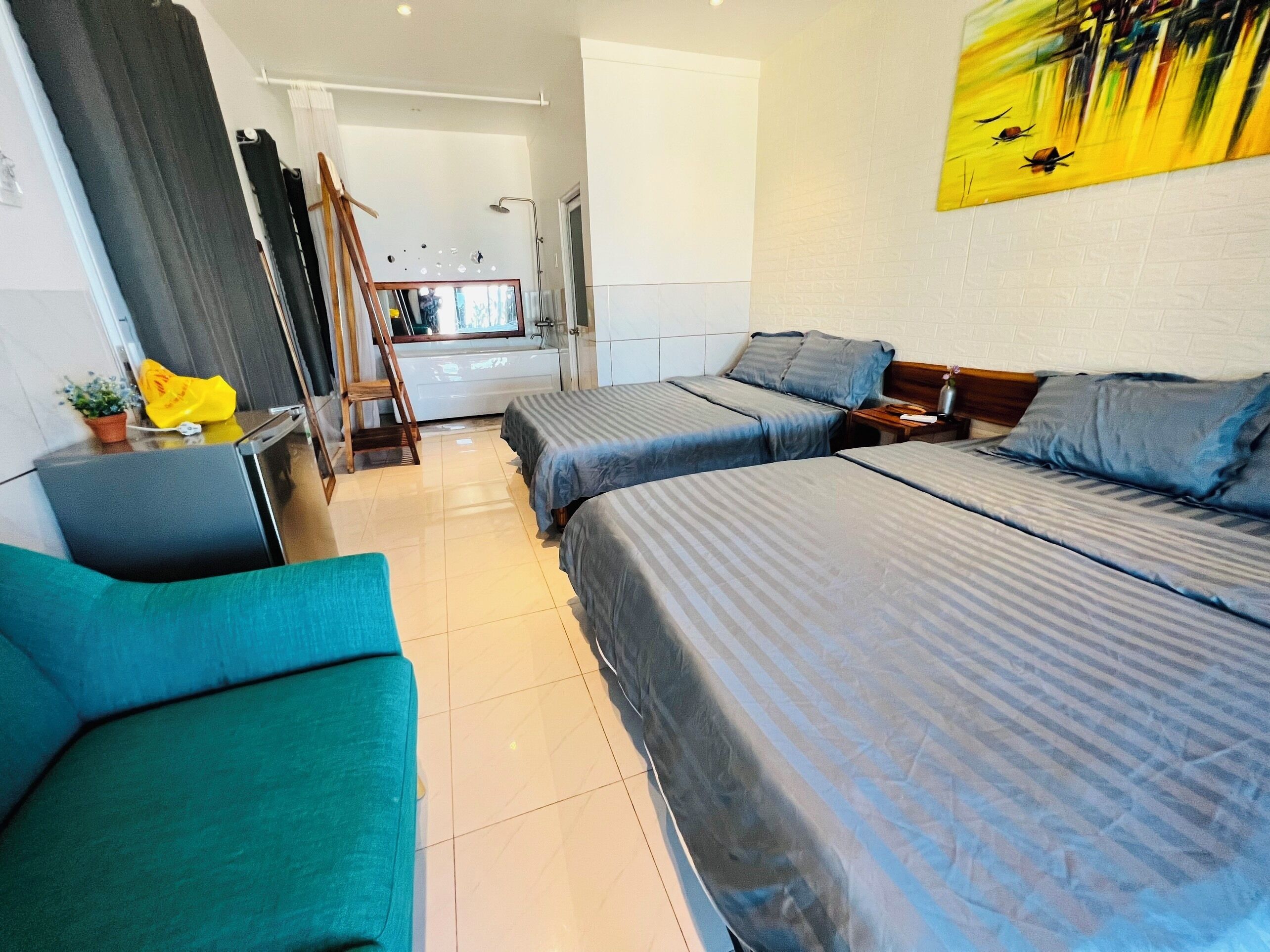 Habitación de hotel con dos camas, un sofá, un cuadro en la pared y un baño visible a través de una puerta abierta.