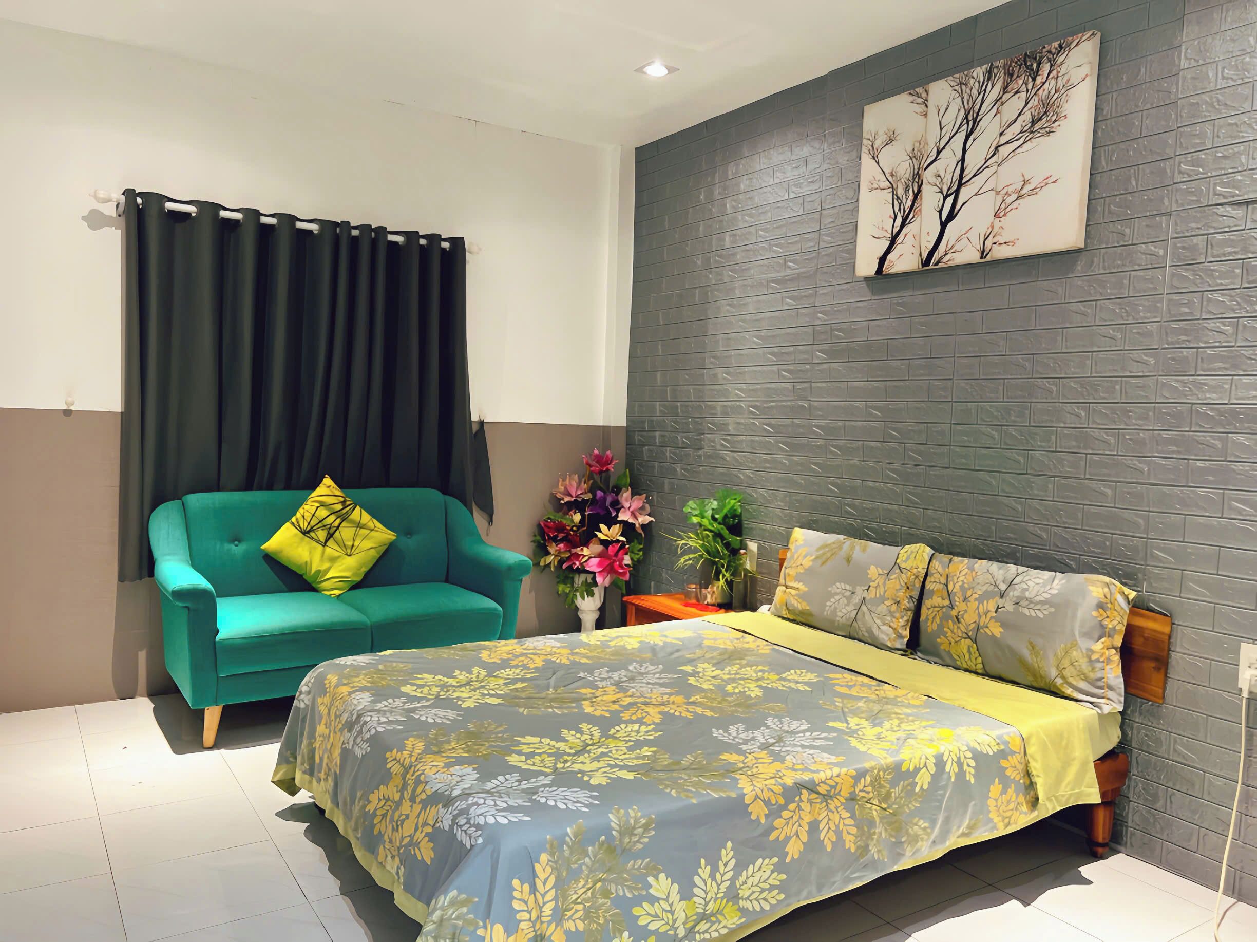A bedroom with a bed, a green sofa, a decorative plant, and a wall-mounted painting.