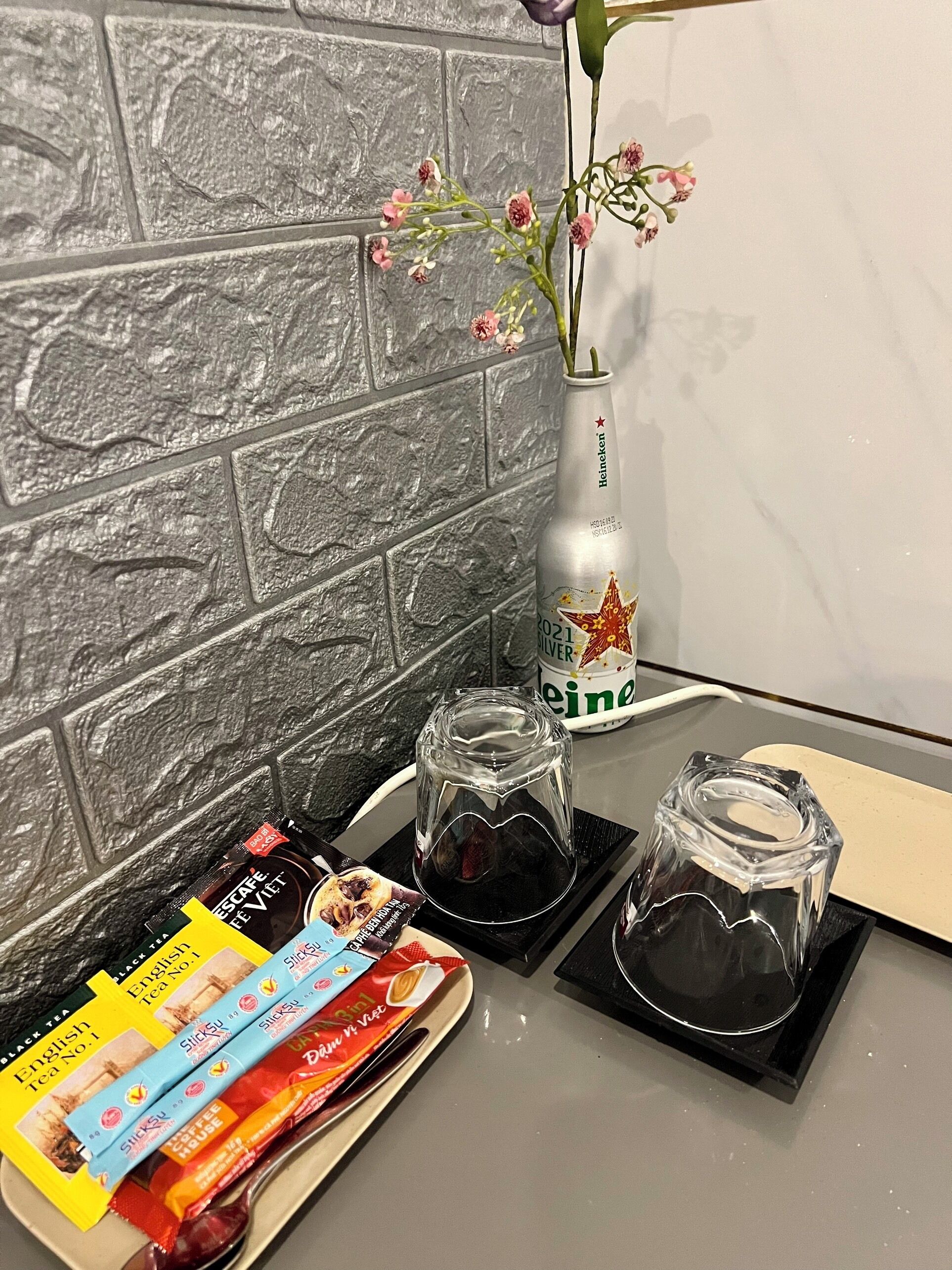 Una encimera de cocina con salpicadero de piedra, una botella de cerveza Heineken, un florero con flores y productos de té y café.