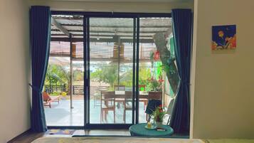 A room with a sliding glass door leading to an outdoor area with a table and chairs, a potted plant, and a view of greenery.