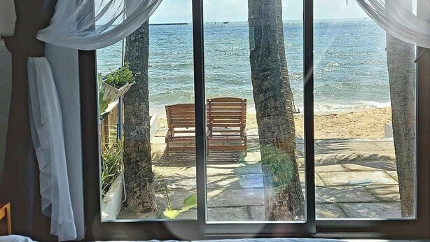 A room with a large window overlooking a beach with palm trees and a bench. - SOHO HOMESTAY PHU QUOC (Phu Quoc)