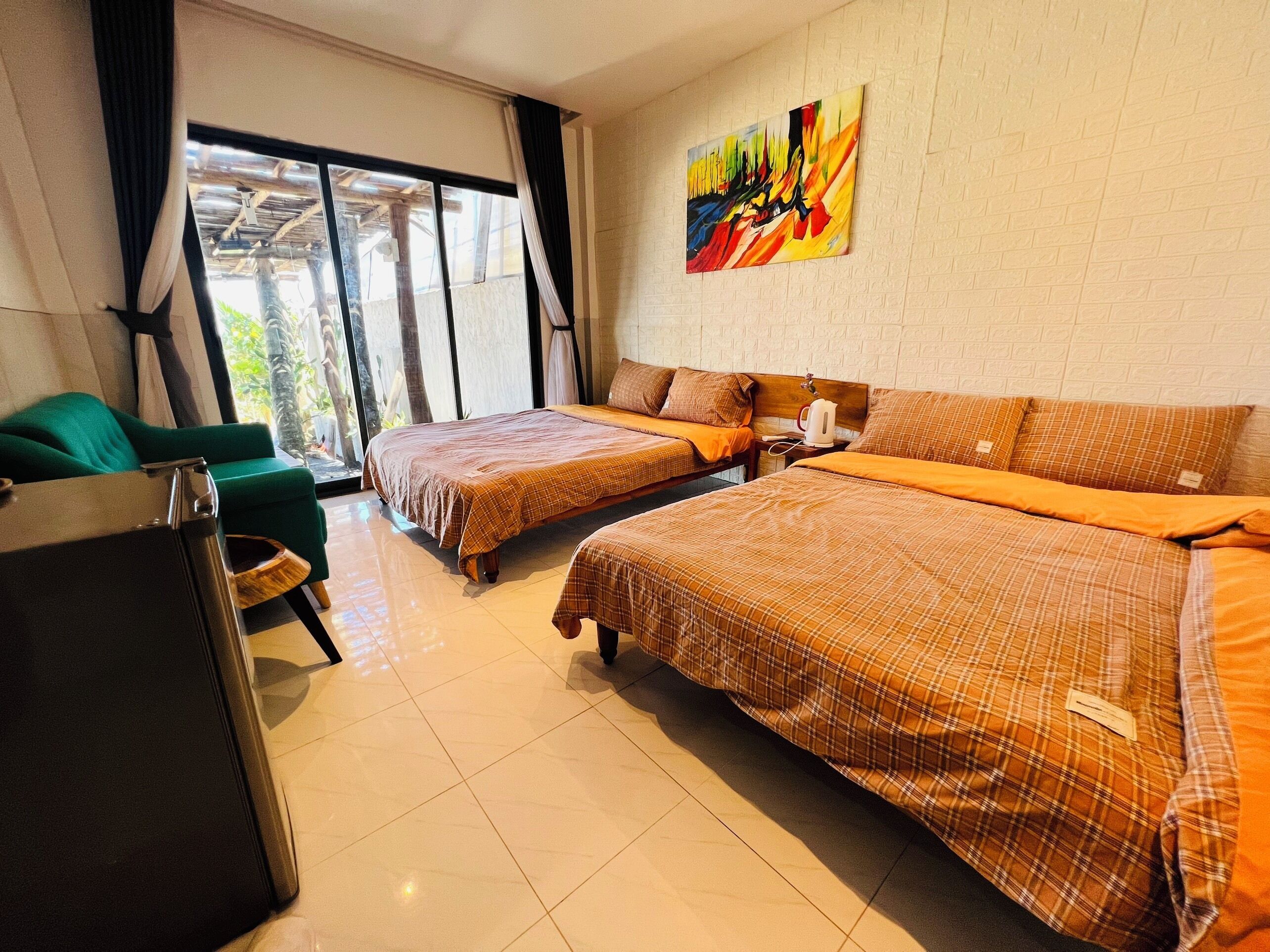 A hotel room with two beds, a green armchair, a large window, and a colorful abstract painting on the wall.