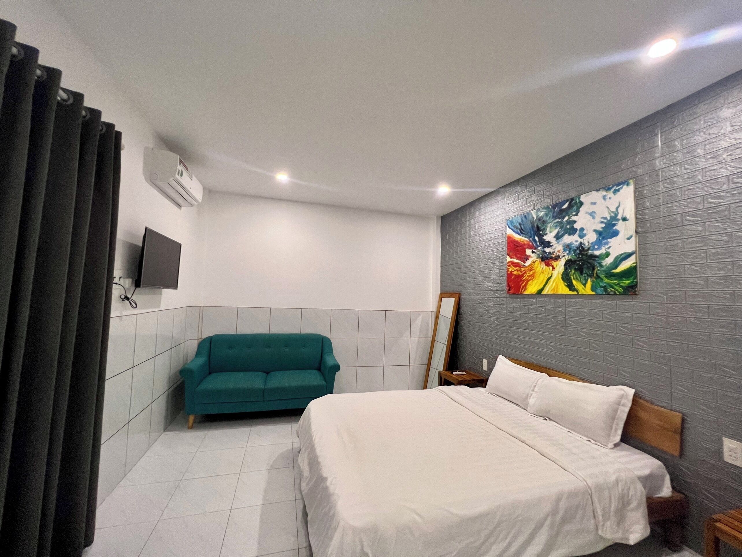 A bedroom with a bed, a teal sofa, a painting, and a TV.