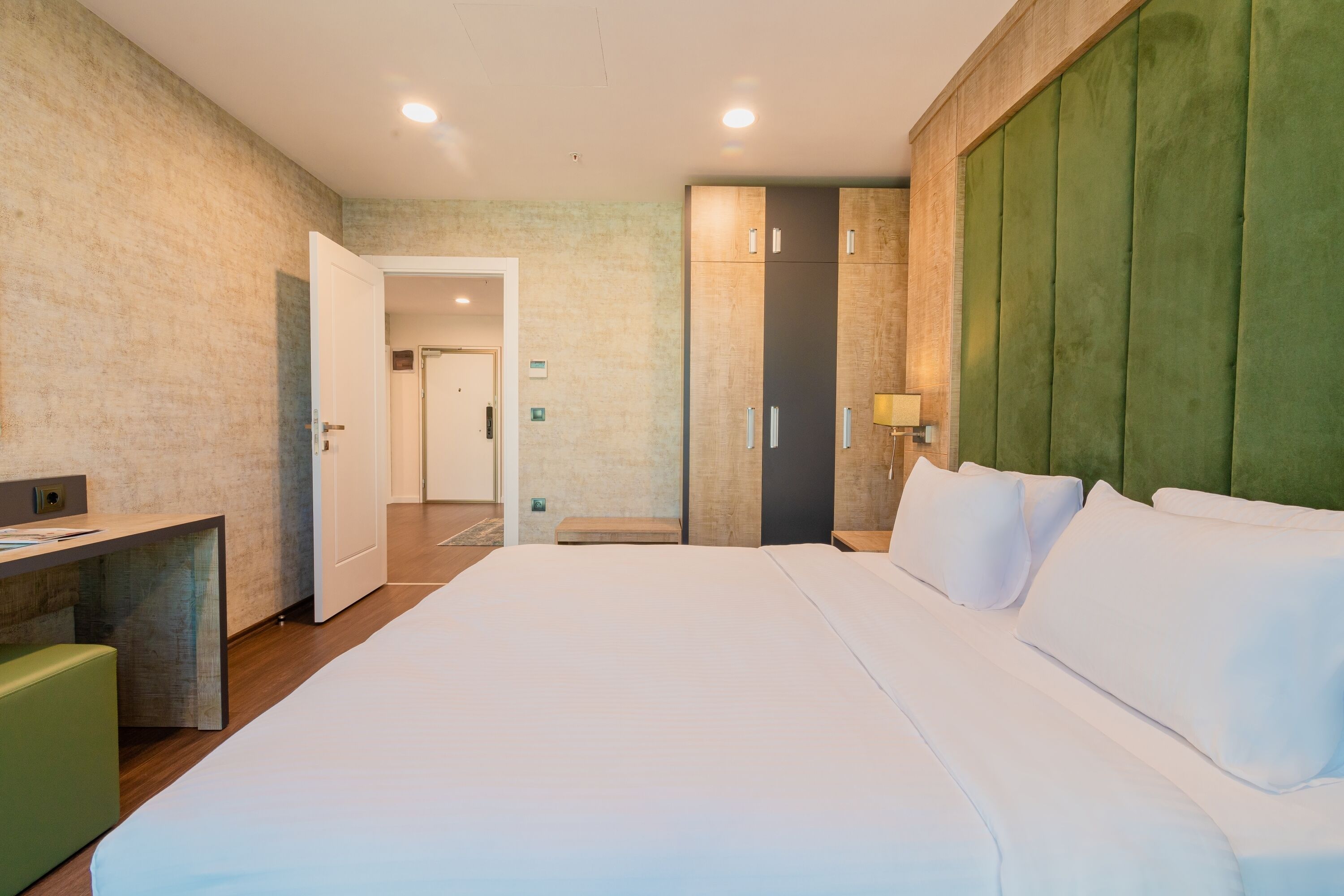Una habitación de hotel moderna con una cama grande, un escritorio y una zona de estar verde.