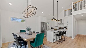 A modern kitchen with white cabinets, a stainless steel refrigerator, and a wooden dining table with chairs. - 4 King Luxury MTN Home | 3 min Downtown Black MTN | 17 min to Asheville (Black Mountain)