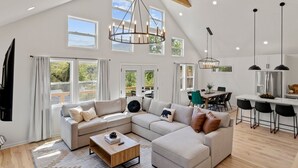 A spacious living room with a large L-shaped sectional sofa, a wooden coffee table, and a dining area with a kitchen in the background. - 4 King Luxury MTN Home | 3 min Downtown Black MTN | 17 min to Asheville (Black Mountain)