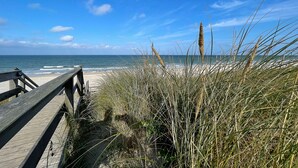 A wooden boardwalk leading to a beach with tall grasses and the ocean in the background. - Apartment Ocean Suite (Wenningstedt)