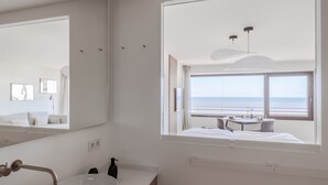 A modern bathroom with a large mirror, a sink, and a window overlooking the sea. - Apartment Ocean Suite (Wenningstedt)