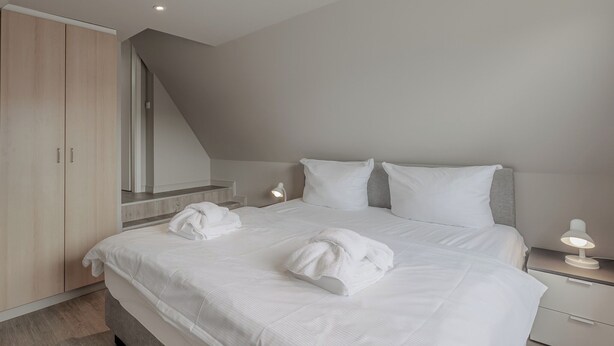 A modern bedroom with a large bed, a wardrobe, and a bedside table with a lamp. - Appartement Hummer (Westerland)
