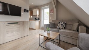 A modern living space with a kitchen, a flat-screen TV, a sofa, and a coffee table. - Appartement Hummer (Westerland)