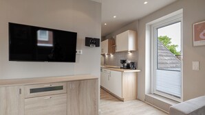A modern kitchen with a flat-screen TV, wooden cabinets, and a large window. - Appartement Hummer (Westerland)
