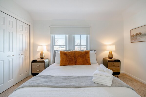 A bedroom with a bed, two bedside tables with lamps, a window, and a door.