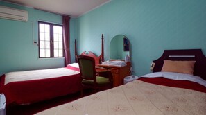 Ein Hotelzimmer mit zwei Betten, einem Schreibtisch, einem Stuhl, einem Spiegel und einem Fenster mit Vorhängen.